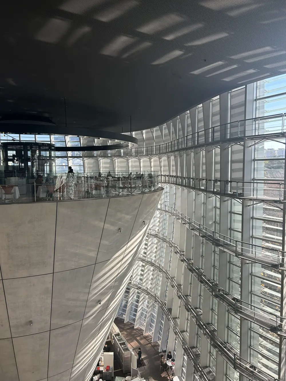 Inside a museum with a rippling glass curtain wall, light patterning the ceiling above a concrete cone that holds a café at its top.