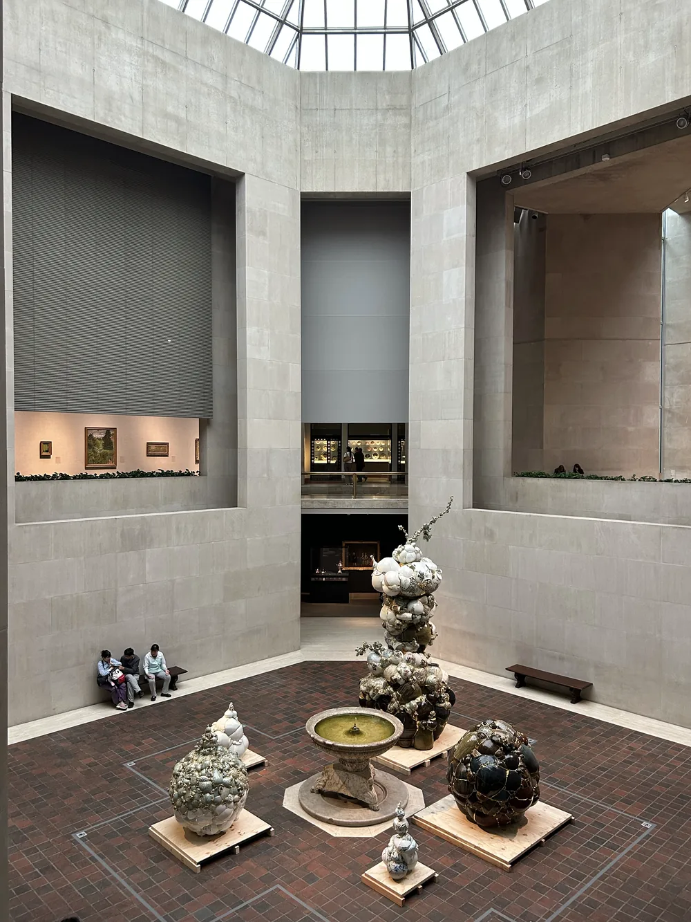 A tall stone-clad museum atrium under a skylight, with ceramic sculptures arranged around a small fountain on the brick floor.